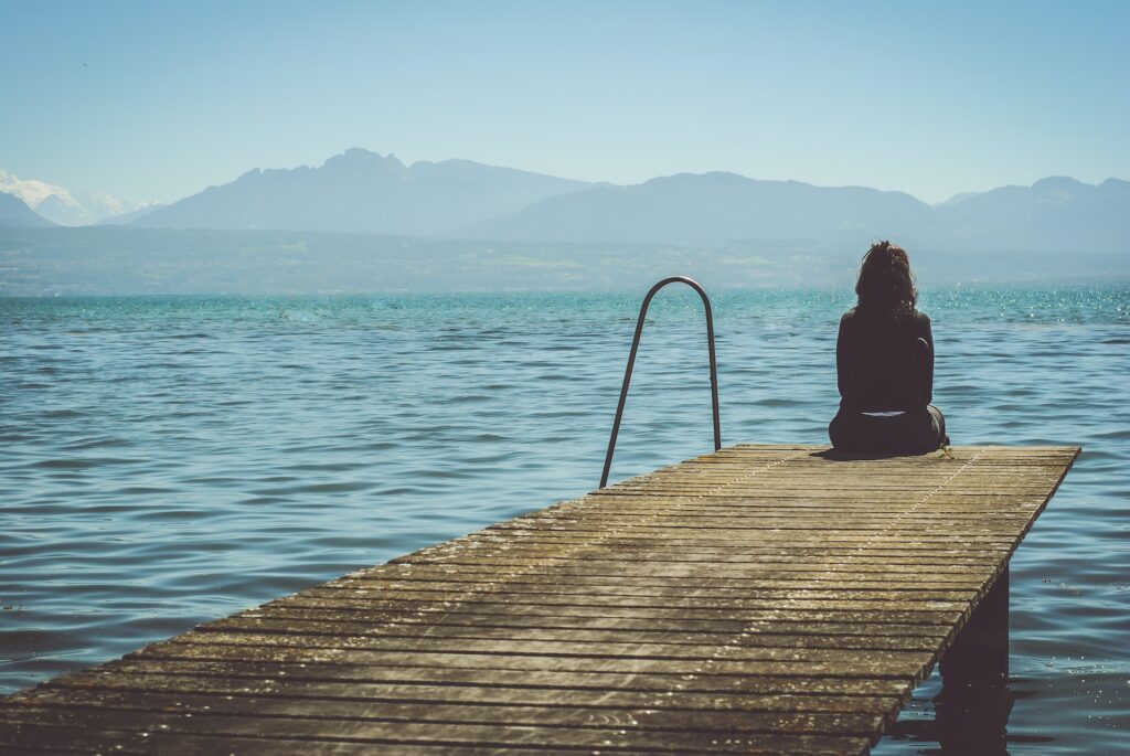 Woman sitting on a jetty looking out over a body of water.